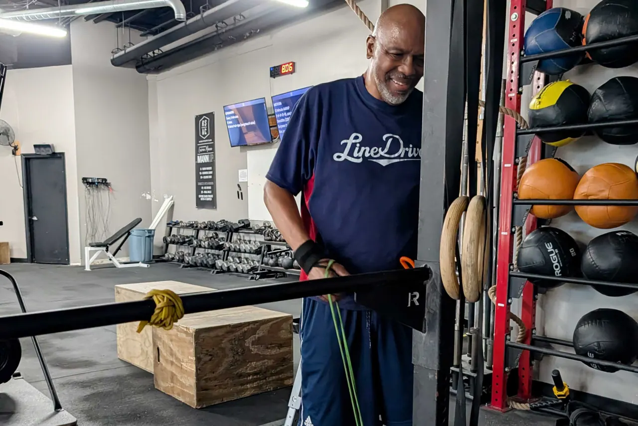A man smiles beside gym equipment.