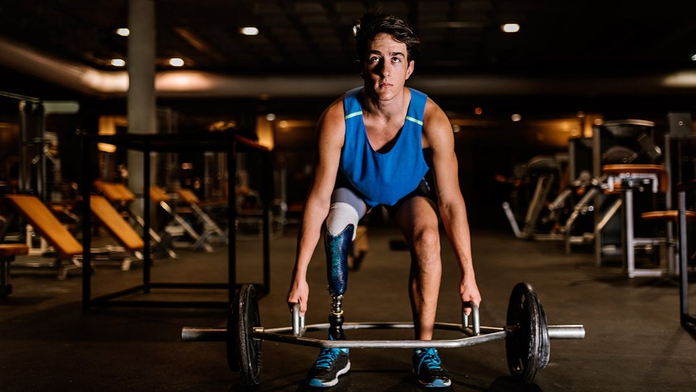 An athlete with a leg prosthesis lifts a barbell in a gym.