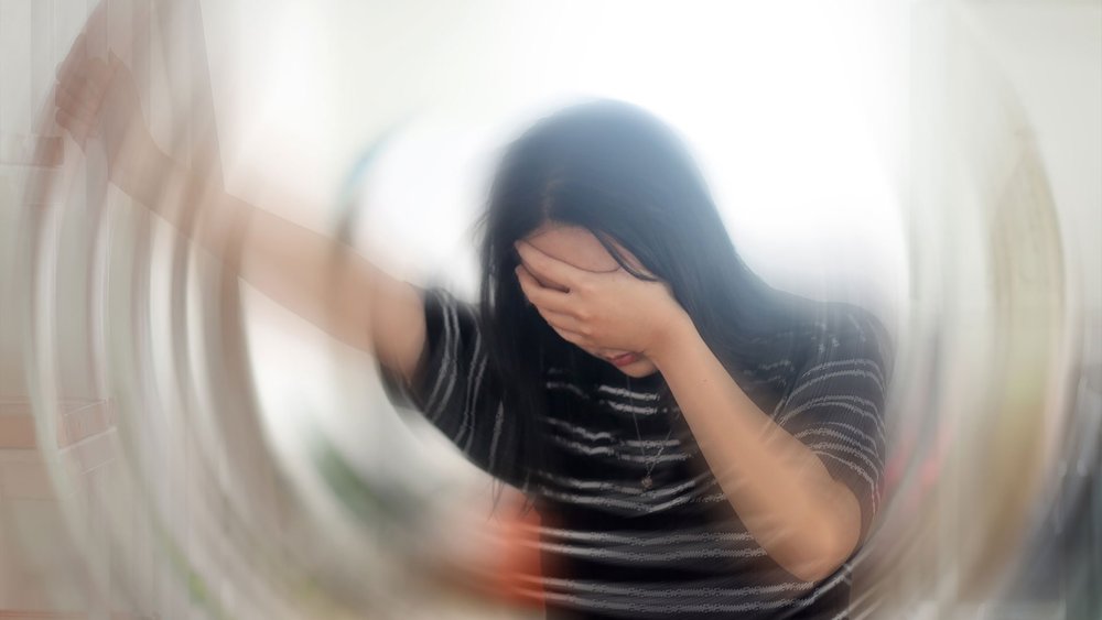 A blurred, spinning view of a person holding their head.