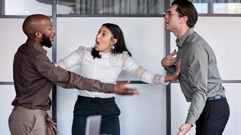 A woman holds back two men who appear to be in a heated argument indoors.