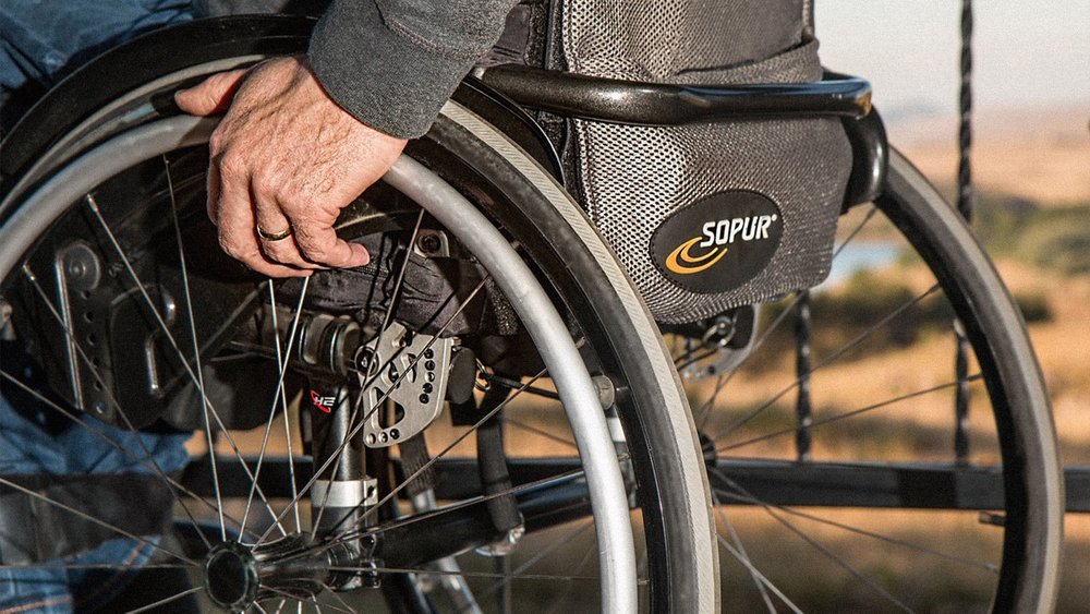 A close-up of a hand gripping a wheelchair's wheel beside a mounted gear bag.