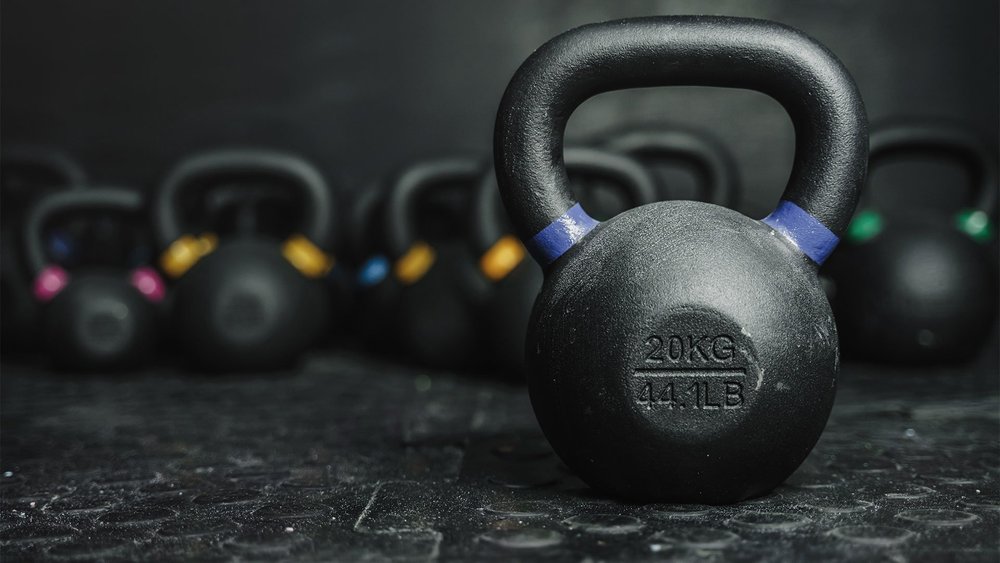 A kettlebell on a gym floor in front of a rack of others.