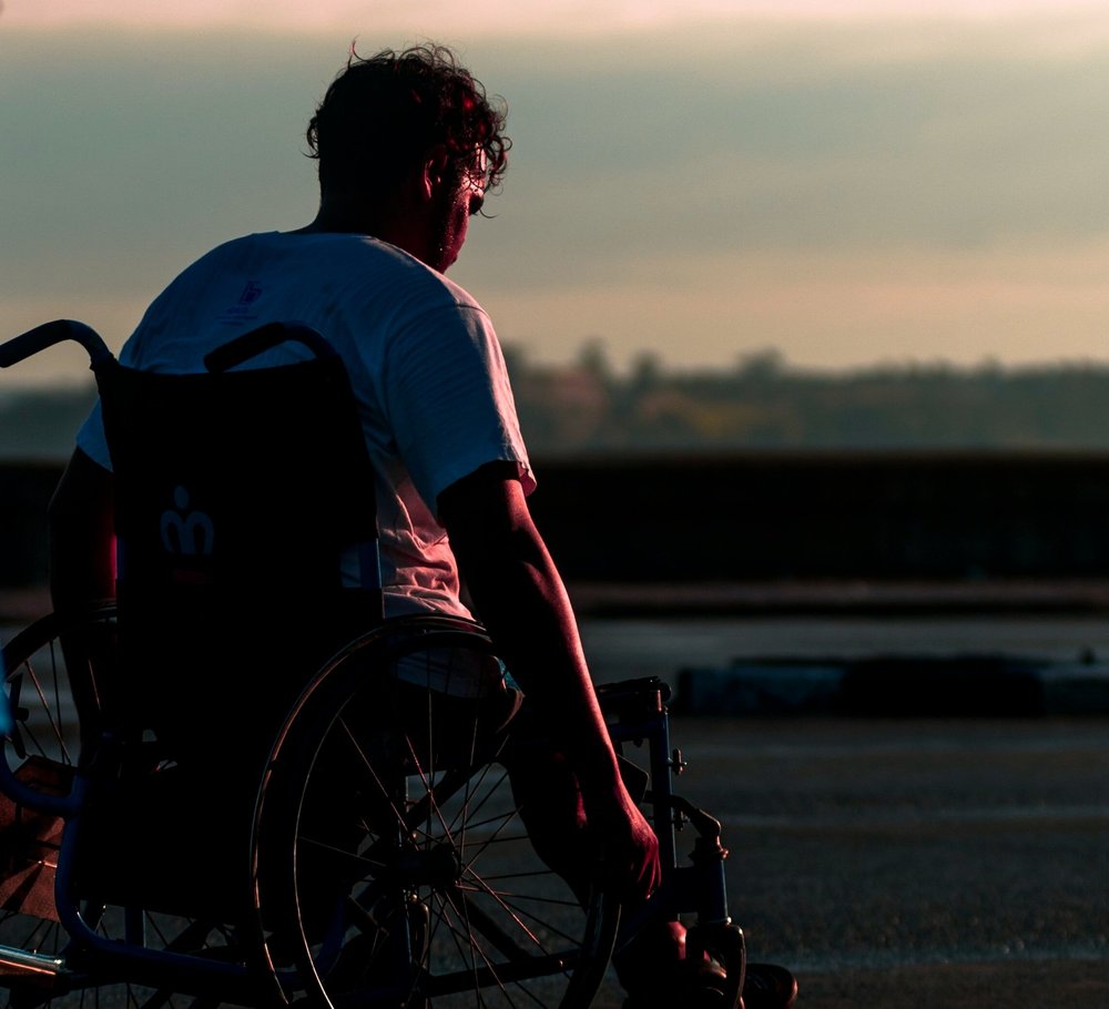 A man in a wheelchair is silhouetted against a colorful sunset sky.