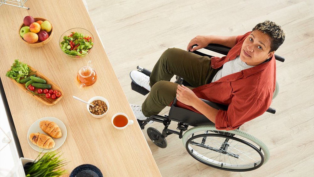 An overhead view shows a woman in a wheelchair at a counter with breakfast foods.