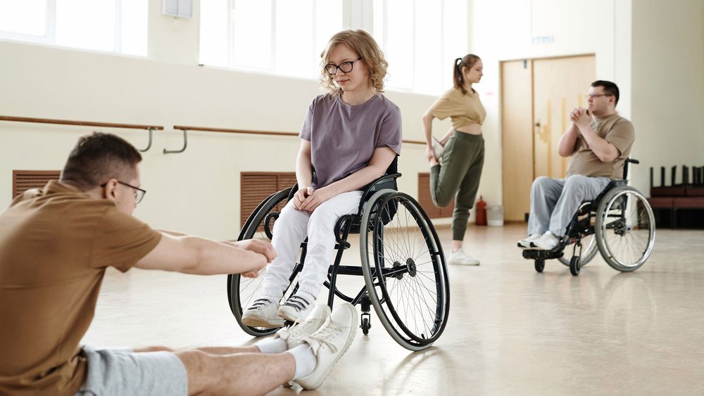 People stretch together in a bright studio, one of them using a wheelchair.