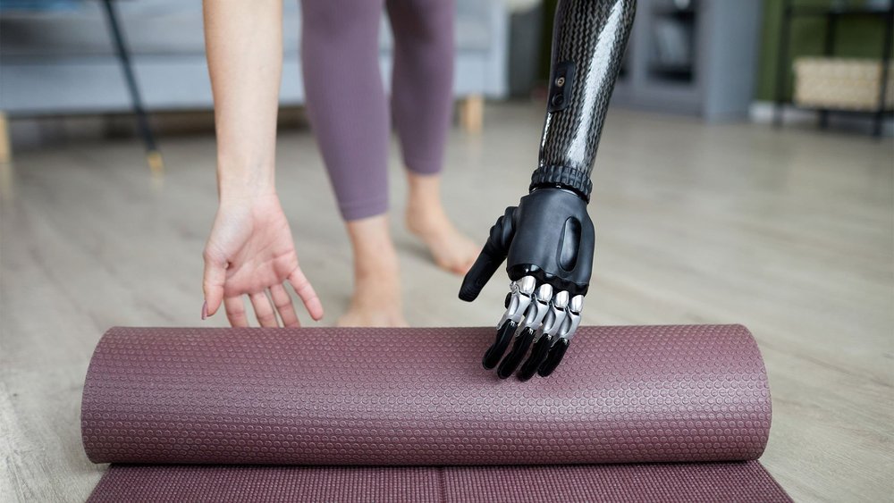 A person with a prosthetic hand unrolls an exercise mat.
