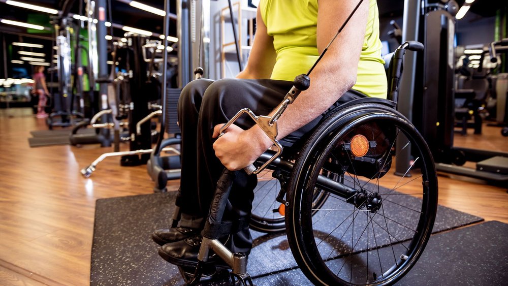A man in a wheelchair uses a cable pulley machine at the gym.