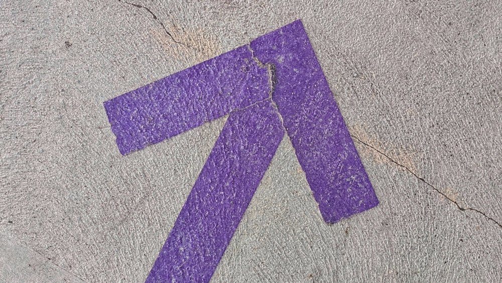 A cracked purple accessibility arrow marking is painted on concrete pavement.