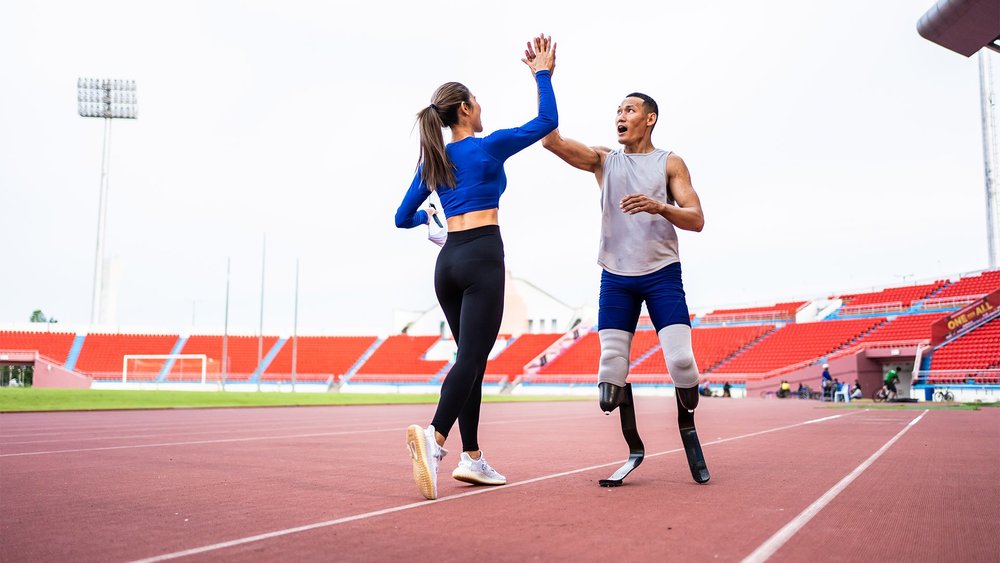 A woman and a man with running blade prosthetics high-five on a track.