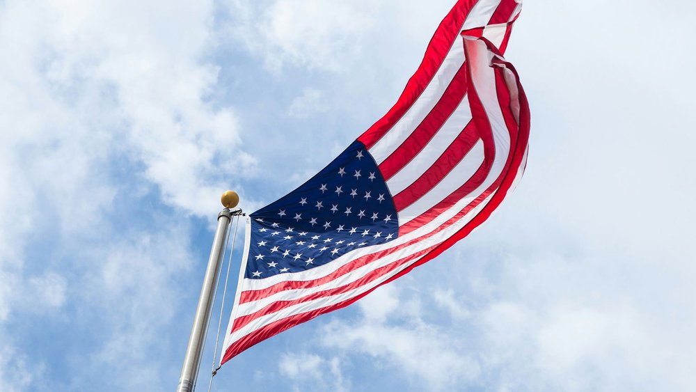 A United States flag flying against a cloudy sky.