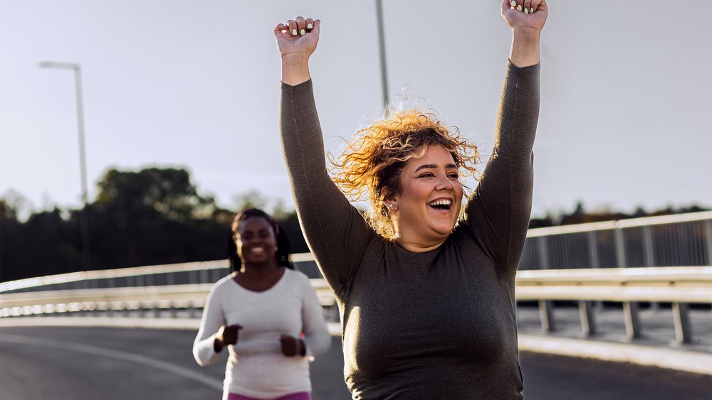 A woman raises her arms in celebration while jogging with another woman behind her.