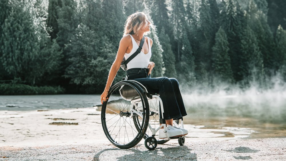 A woman in a wheelchair beside misty water at the edge of a forest.