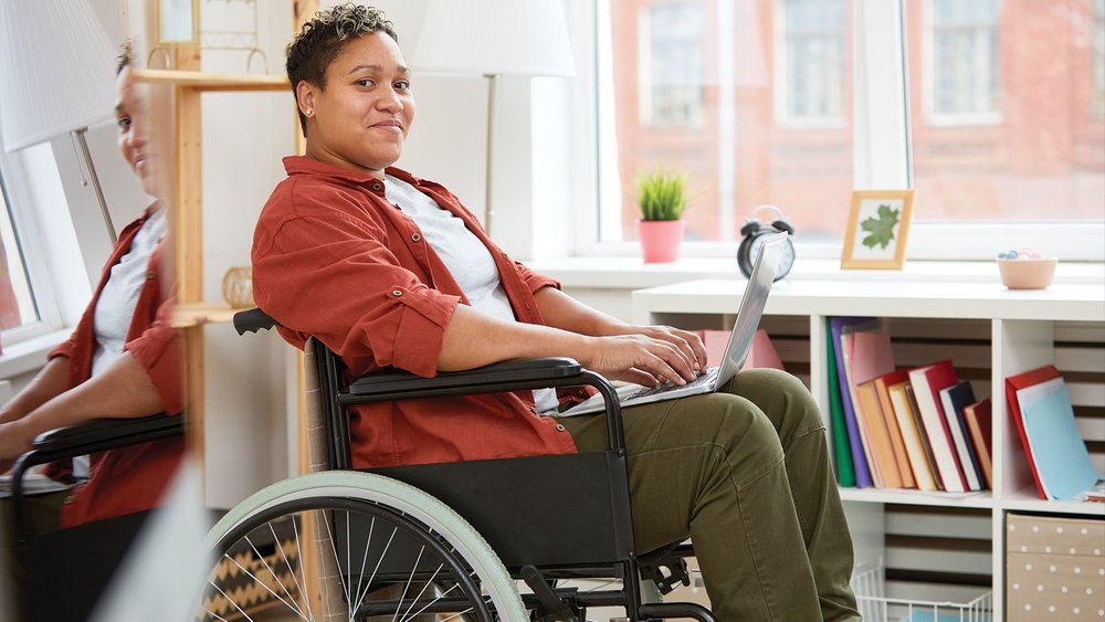 A woman in a wheelchair sits in a room lined with bookshelves.