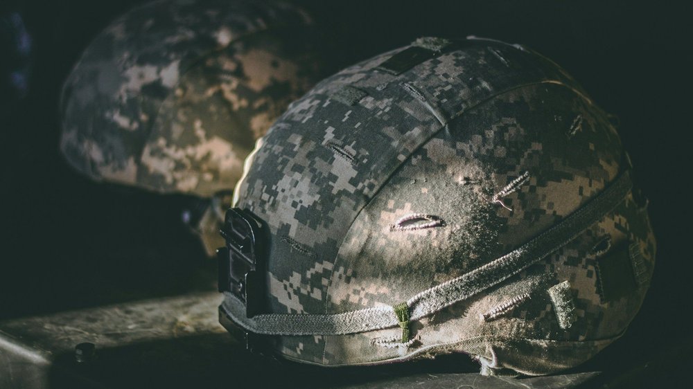Two camouflage military helmets rest together in dim, low light.