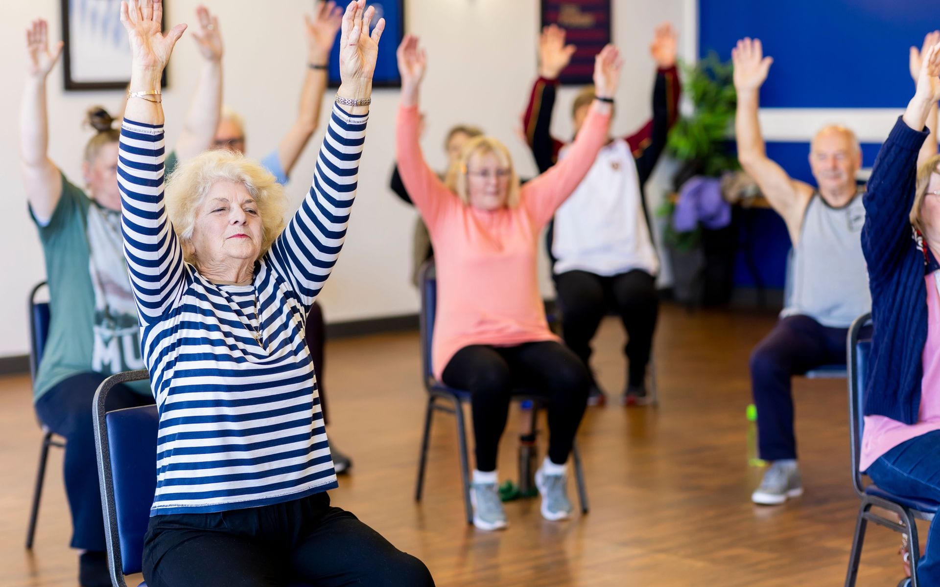 Older adults raising their arms during a seated group exercise class.