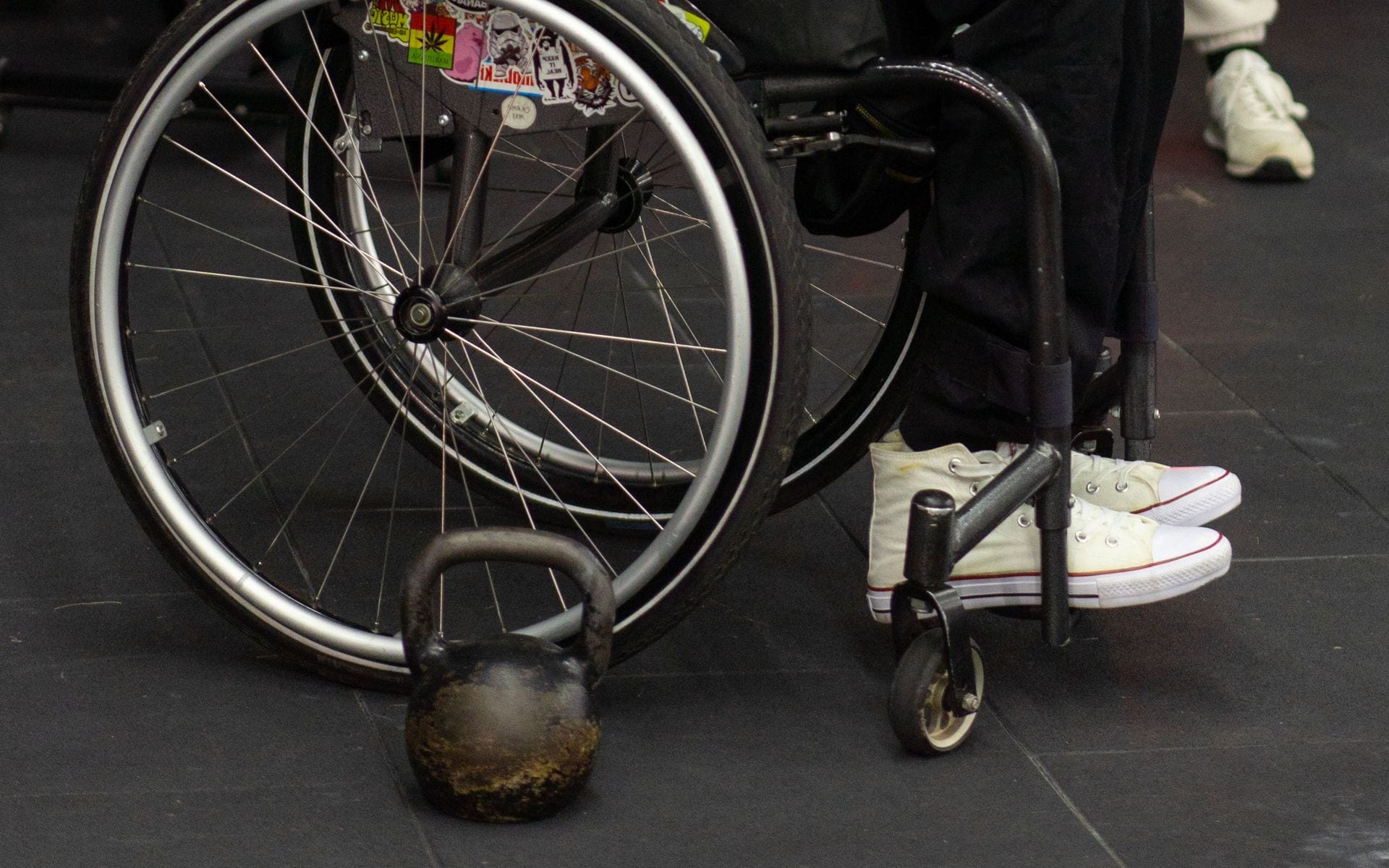 A wheelchair and kettlebell on the floor of a gym.