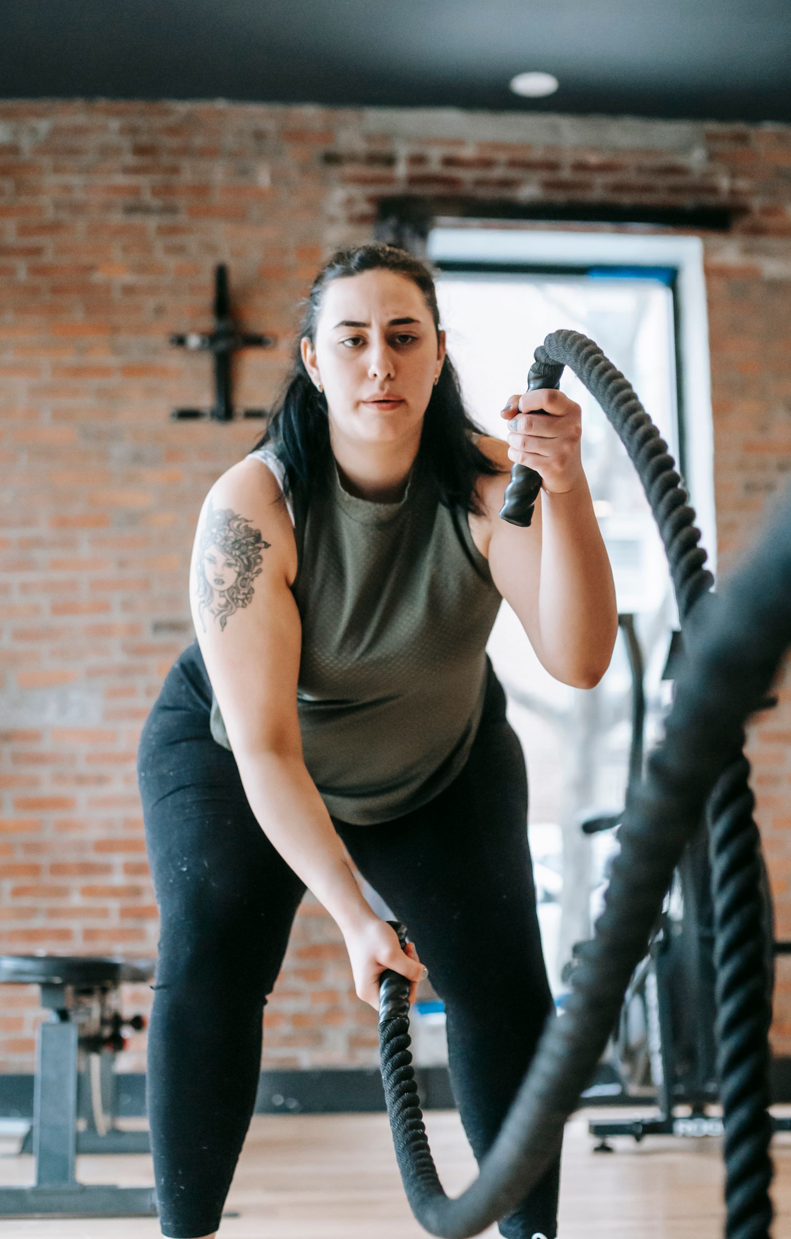 A woman swings battle ropes in a brick-walled gym.